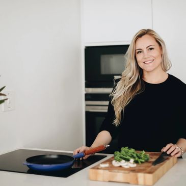 Smiling woman cooking in a modern kitchen with fresh vegetables.