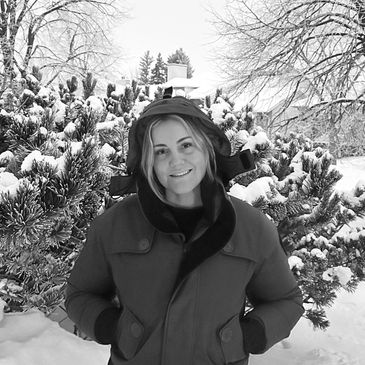 Smiling woman in a hooded winter jacket stands in snowy landscape.