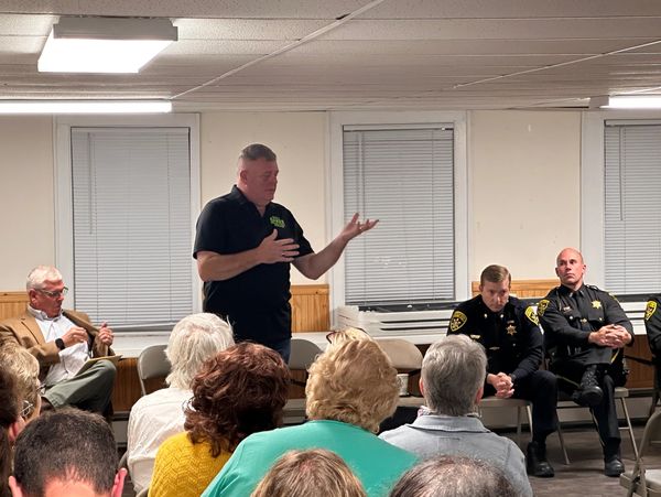 A man speaks to a seated audience with police officers and others listening attentively.