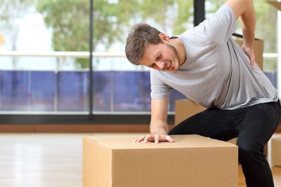 man holding hurt back while picking up a box