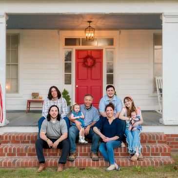 Happy family sitting on front porch steps with red door background.