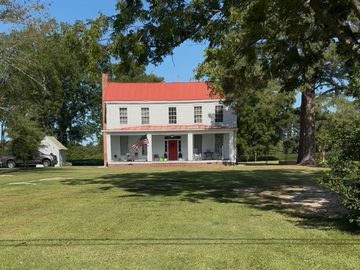 A two-story white house with a red roof and porch in a large grassy yard.