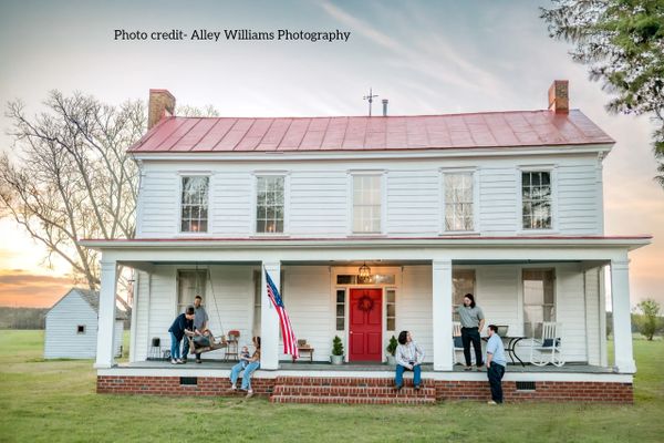 Family gathered on the porch of a charming white farmhouse at sunset.