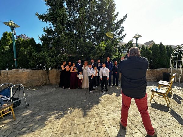 A photographer captures a wedding party posing outdoors in front of a large tree.