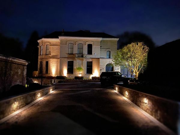 A large, well-lit house at night with illuminated driveway and tree.