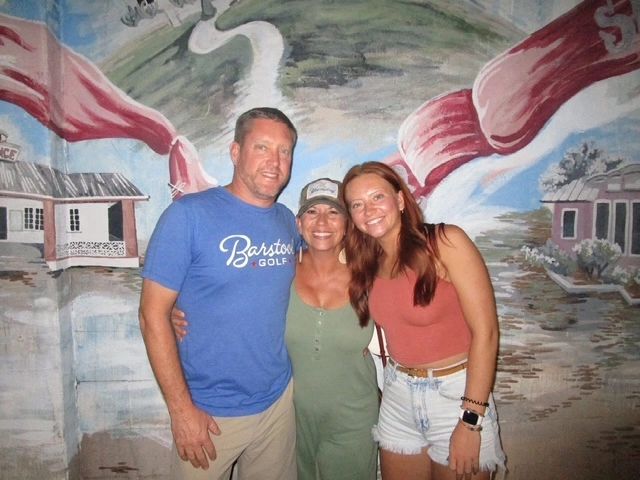 Three people posing in front of a painted mural.