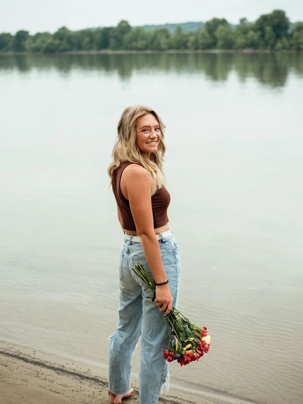 Smiling woman holding flowers by the water.