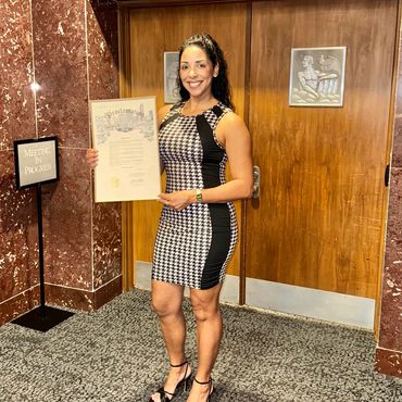 Woman in patterned dress holding a certificate and smiling indoors.