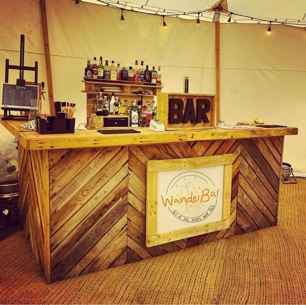 Rustic wooden bar setup with bottles and a sign reading 'WanderBar'.