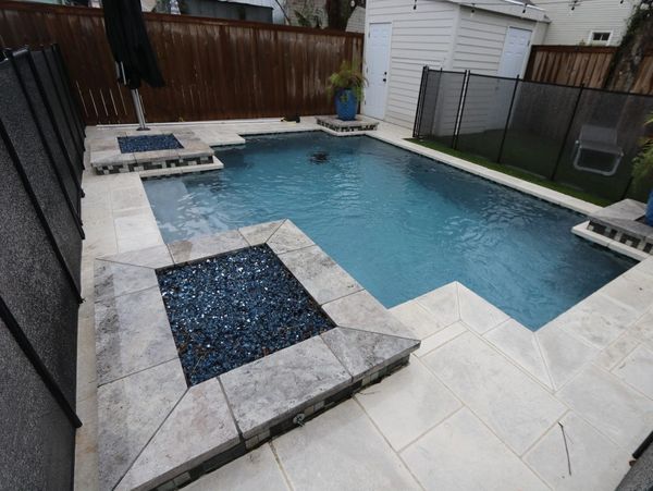 Piscine creusée moderne en béton avec foyer intégré, patio en pierre et clôture de sécurité