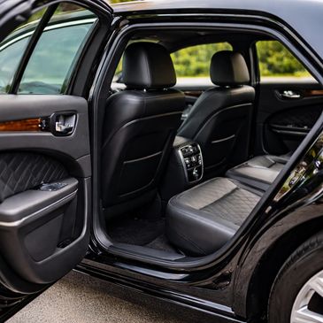Open rear door showing black leather car seats and interior with wood accents.