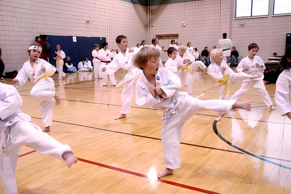 Many children are visible, all wearing white martial arts uniforms (doboks) with yellow belts
