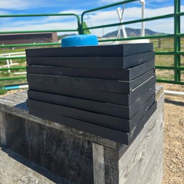 Stacked black rubber mats on a wooden platform outdoors under a blue sky.