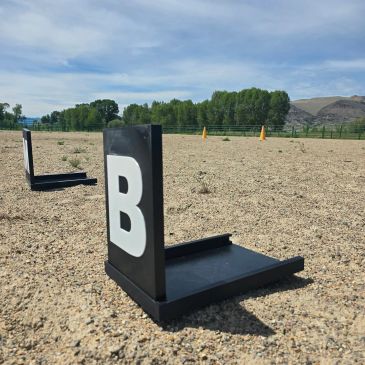 Black bookends with letters on gravel under a blue sky.