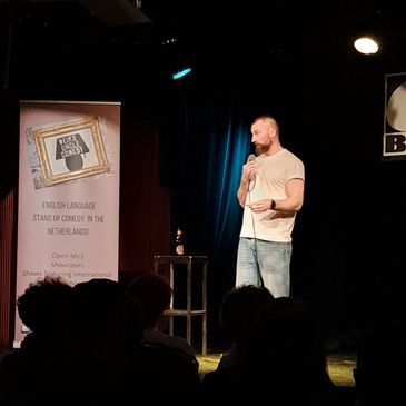 Comedian performing stand-up comedy on stage with microphone.