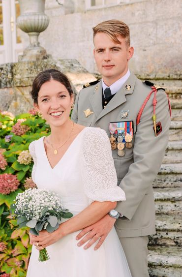 Couple marié avec mari militaire posant devant des escaliers en pierre.