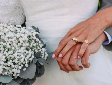 Mains d'un couple marié avec bouquet de fleurs blanches.