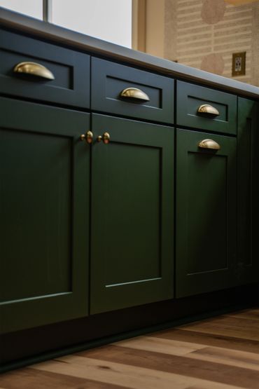 Dark green kitchen cabinets with brass handles and wooden floor.