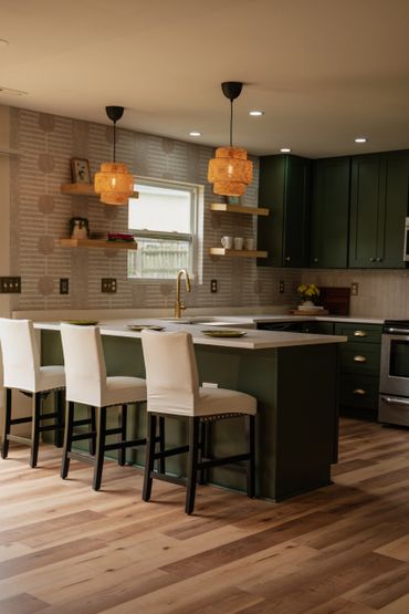 Modern kitchen with green cabinets and white bar stools under warm pendant lights.