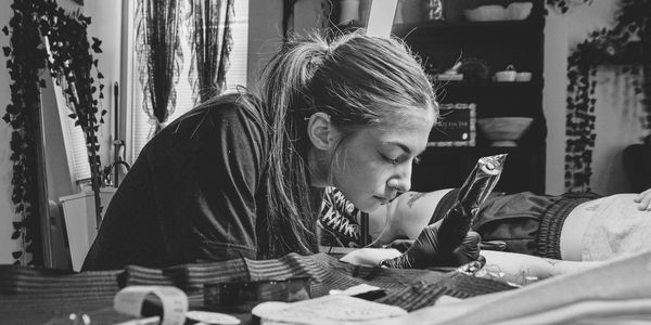A focused tattoo artist working on a client's leg in a cozy studio.