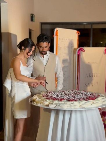 A couple cutting a large wedding cake together indoors.