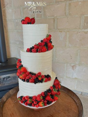 Three-tier white wedding cake adorned with fresh berries and a 'Mr &amp; Mrs' topper.