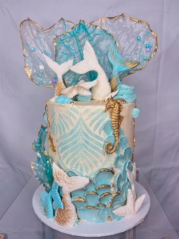 Elegant ocean-themed cake with mermaid tails and seahorses.