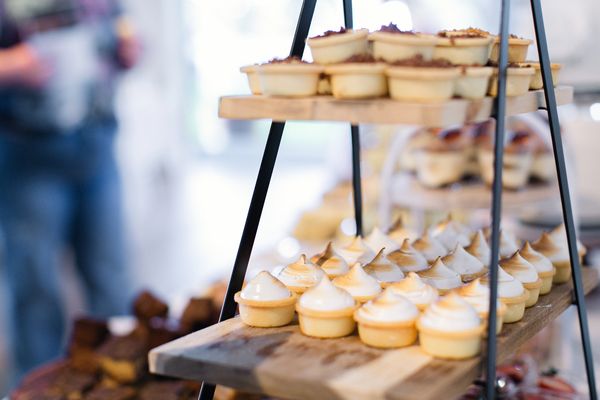 Mini tarts with meringue topping displayed on wooden shelves.