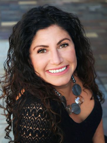 Smiling woman with curly hair and statement necklace.