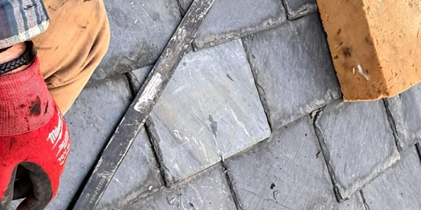 Worker's hand with red glove laying slate tiles with a brick and straight edge tool.