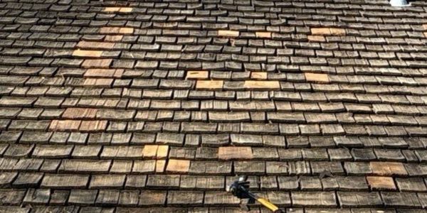 A roof with wooden shingles, some replaced with new lighter ones, and a hammer lying on it.