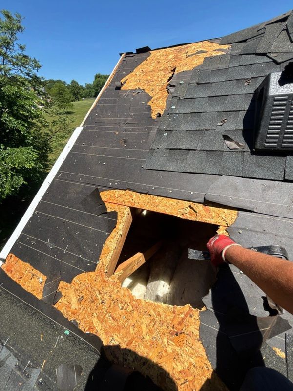 Damaged roof with missing shingles and exposed underlayment being repaired.