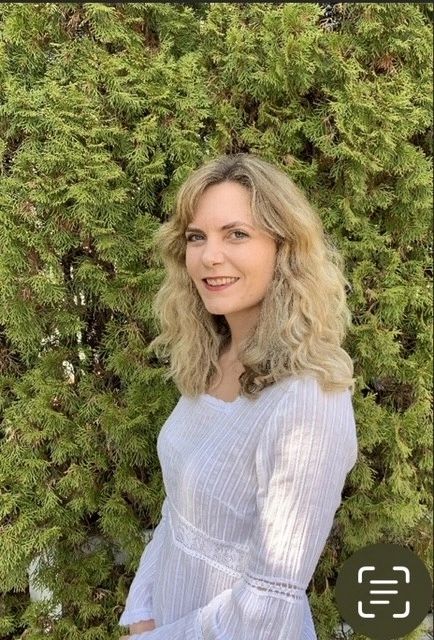 Woman in white dress standing outside near green bushes.