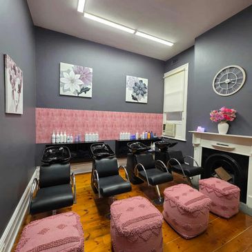 Modern salon with black washing chairs and pink ottomans on wooden floor.