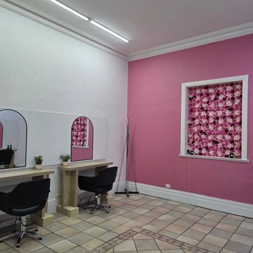 A stylish salon corner with black chairs, wooden tables, and a pink floral wall accent.