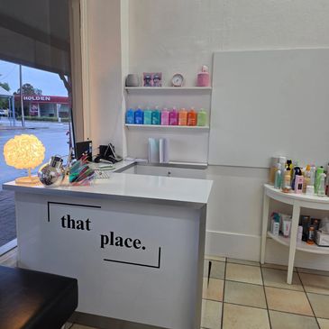 Reception desk with 'that place.' sign and colorful bottles on shelves.