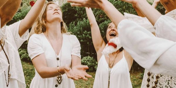 Women in white dresses joyfully reaching upwards outdoors.