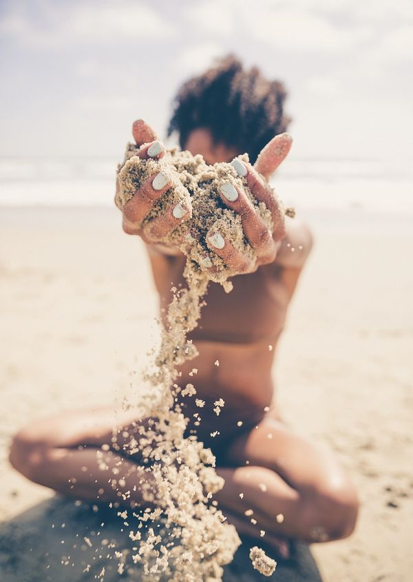 Person sitting on the beach letting sand fall through their hands.