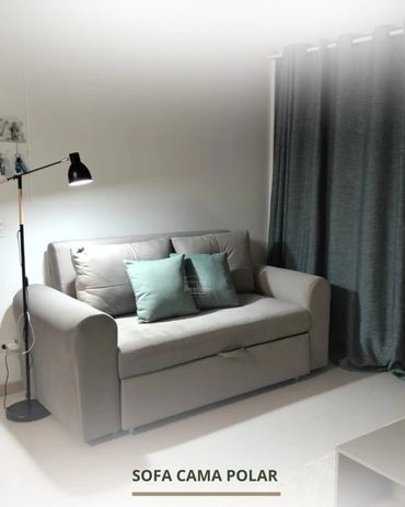 Modern gray sofa bed with teal cushions and a floor lamp in a minimalist room.