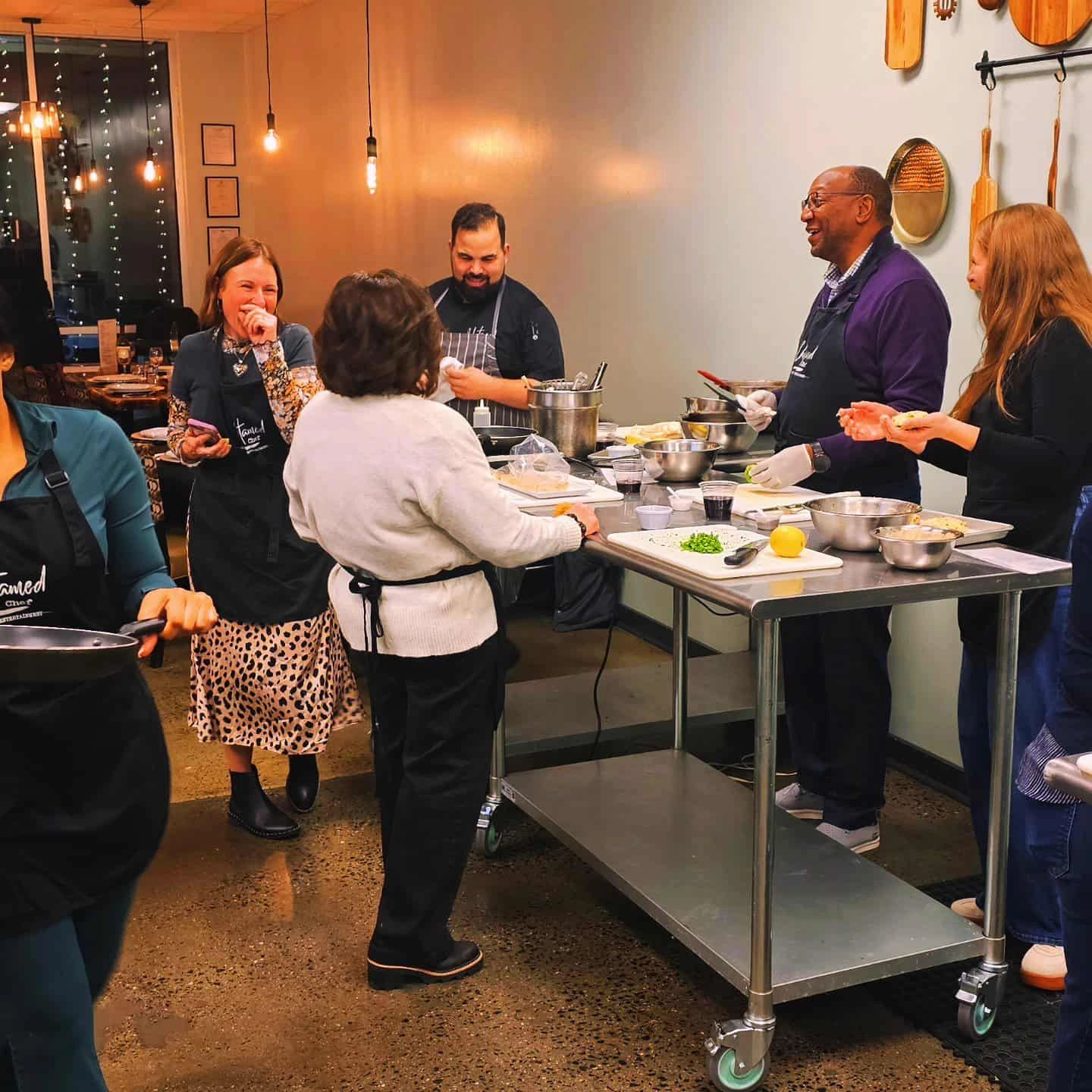 Group cooking class with people laughing and preparing food together.