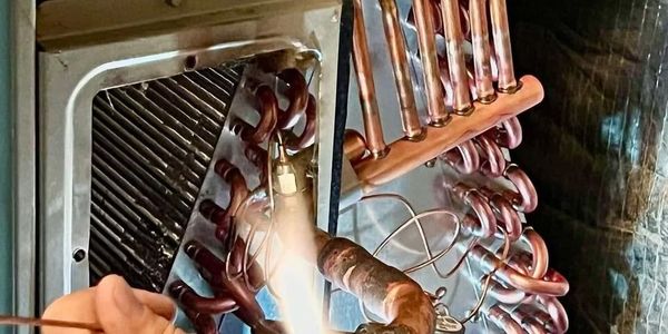 Close-up of a technician soldering copper pipes in an HVAC unit.