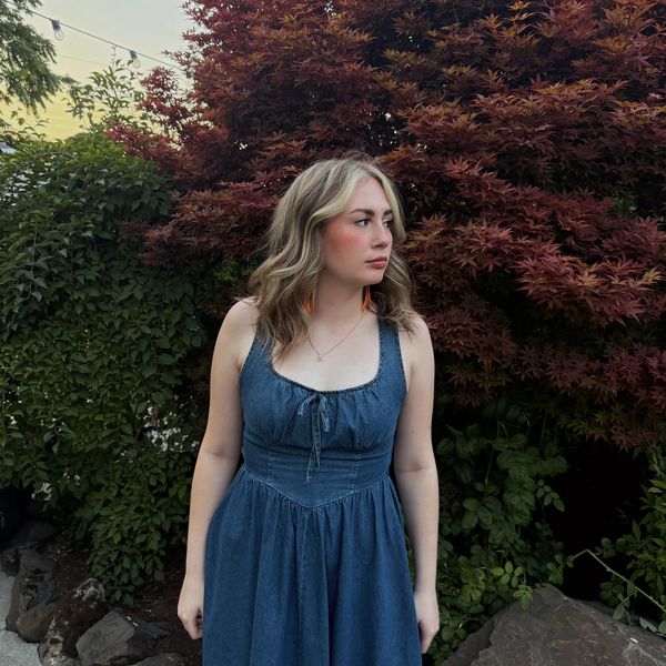 A woman in a denim dress standing near autumn foliage.