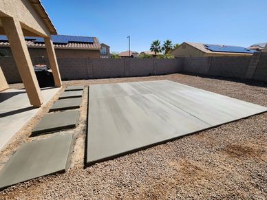 Freshly poured concrete slabs in a backyard under a clear sky.