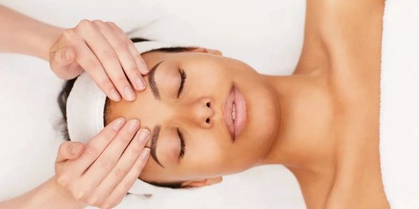 A woman receiving a relaxing facial massage with eyes closed.