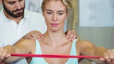 A woman exercises with a resistance band while a man assists her shoulder movement.