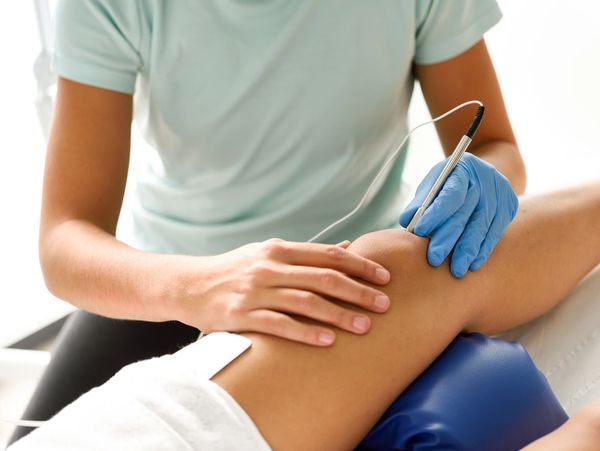 Therapist performing electrotherapy on a patient's knee.