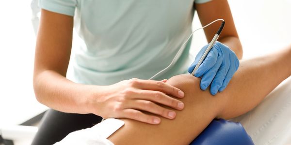 Physical therapist using an ultrasound device on a patient's knee for treatment.