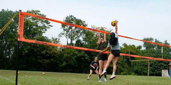 Two women playing outdoor volleyball, one blocking and one spiking the ball.