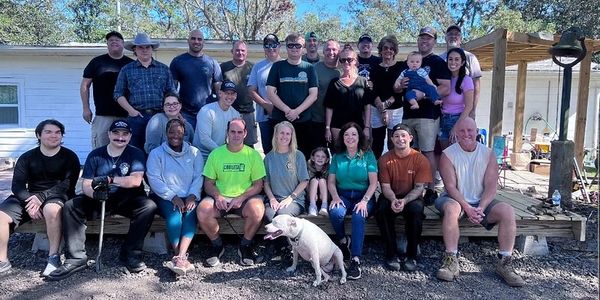 Large group of people gathered outdoors in front of a house with a dog.