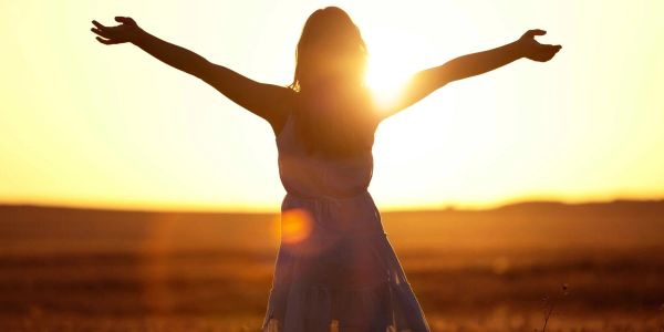 Silhouette of a woman with arms outstretched at sunset in a field.